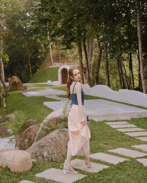 Creator wearing a teal top and striped skirt in a garden